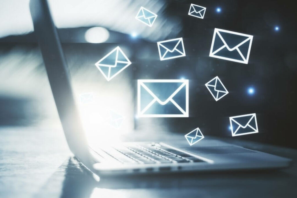 Abstrakcyjna grafika przedstawiająca email marketing: przychodzące wiadomości w formie kopert lecących w stronę laptopa 