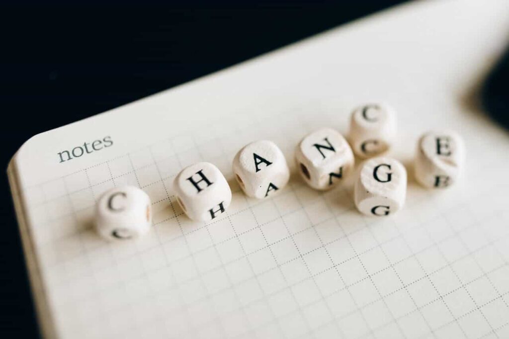 Na kartce notatnika leżą kostki z literami tworzącymi słowo „change” – nawiązują one do zarządzania zmianą