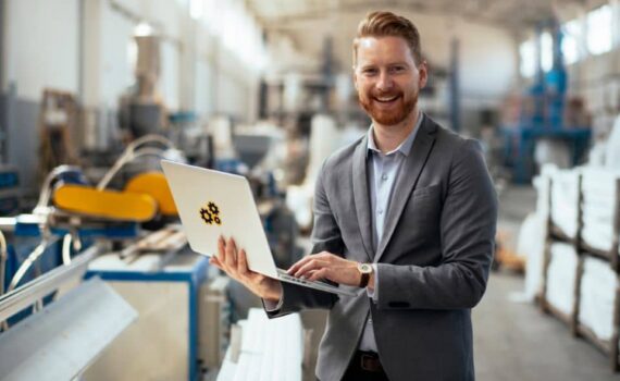 Obrazek wyróżniający przedstawiający mężczyznę z laptopem w fabryce